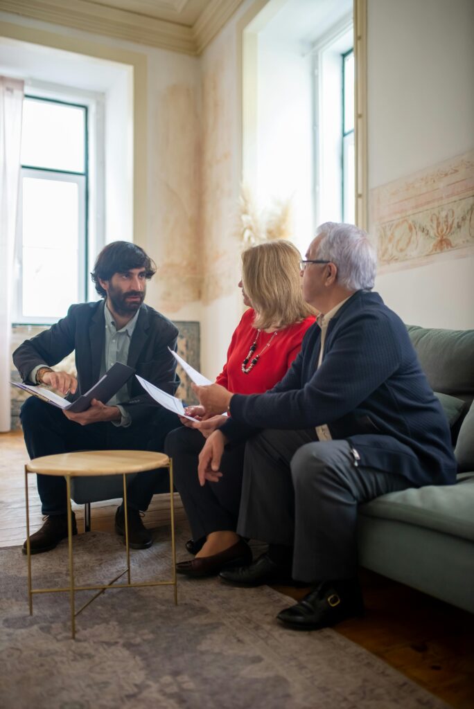 An advisor discussing financial documents with a senior couple indoors in a cozy living room setting.